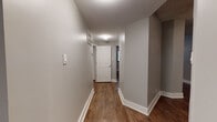 This single-floor space presents a cohesive, updated interior unified by dark hardwood-style flooring and neutral grey walls throughout. White baseboards provide clean contrast, contributing to a polished, well-maintained aesthetic.

The layout flows from a straightforward entry hallway, lit by a flush-mount ceiling fixture, leading to the main living areas. The open living and dining areas are generously sized, each equipped with ceiling fans and textured ceilings. Multiple windows dressed with horizontal blinds allow natural light to filter in, brightening the grey-toned walls.

The kitchen is thoughtfully appointed with white shaker-style cabinetry, granite-look countertops, a stainless steel sink, and stainless appliances including a dishwasher and range. An integrated open shelving unit provides additional storage and display space alongside a pantry door.

The bedroom areas are well-proportioned, each featuring ceiling fans, textured ceilings, and windows offering natural light. The bathroom is cleanly designed with a white vanity, granite countertop, framed mirror, brushed nickel fixtures, and a tub-and-shower combination with a glass door. The consistent flooring and neutral palette throughout create a unified, functional living environment.