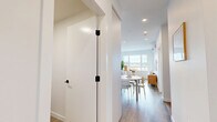 Located at Royal Commons in Victoria, BC, this well-appointed one-bedroom, two-bathroom residence offers a thoughtfully designed layout across a single floor. The open-concept kitchen and living area serves as the heart of the home, featuring a sleek, modern kitchen with flat-panel white cabinetry extending to the ceiling, a tile backsplash, stainless steel appliances including a slide-in range and dishwasher, and black matte hardware accents throughout. Light wood-tone flooring runs consistently across the entire unit, lending warmth and visual continuity. The living room is bright and airy, with large windows framing scenic outdoor views, creating a welcoming and light-filled atmosphere. The bedroom is a serene retreat, complete with a walk-in closet and a window overlooking the same pleasant outdoor scenery. A dedicated office nook provides a practical workspace, ideal for remote work or study. Both bathrooms are finished in a clean, contemporary style with white vanities, black hardware, and one featuring a full soaker tub. A mini-split system provides efficient climate control. Throughout the space, a neutral, minimalist palette of whites and natural wood tones creates a cohesive, modern aesthetic that feels both calm and functional.
