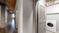 Located at 445 E Illinois St in Chicago's vibrant Streeterville neighborhood, this single-floor loft space masterfully combines historic industrial character with contemporary design. The layout is expansive and open, defined by rich hardwood floors that run throughout and soaring wood-beam ceilings that lend warmth and architectural distinction to every room.

Exposed brick walls are a defining feature, particularly prominent in the bedroom areas, where arched windows frame sweeping views of the Chicago skyline and fill the rooms with generous natural light. The industrial aesthetic is further emphasized by visible ductwork running along the ceilings, complementing the raw structural elements of the space.

The kitchen is a standout highlight, outfitted with full-height dark wood cabinetry, stone countertops, a glass tile backsplash, and a suite of stainless steel appliances including a gas range, built-in microwave, and a large refrigerator. Track lighting mounted to the wood-plank ceiling illuminates the workspace, while light hardwood floors add a warm contrast to the cabinetry.

A hallway with louvered closet doors provides practical storage, connecting the living areas with ease. Throughout the space, the interplay of original brick, natural wood, crisp white walls, and modern finishes creates a dynamic and inviting urban loft atmosphere that is both functional and full of character.