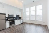 Located in Atlanta's Castleberry Hill neighborhood, this two-story space offers a thoughtfully designed interior with contemporary finishes throughout. The main level is anchored by a generous open living area with soaring ceilings and light wood-tone flooring that runs continuously through the space. Tall, multi-pane windows flood the interior with natural light and provide views of the surrounding neighborhood, enhancing the sense of volume and openness.

The kitchen is well-appointed with white shaker-style cabinetry extending to the ceiling, a dark navy subway tile backsplash, stone countertops, and a full suite of stainless steel appliances including a refrigerator, range, microwave, and dishwasher. A bathroom on the main level features wood-tone flooring, white subway tile in the shower, and clean, minimal fixtures.

A sculptural black spiral staircase serves as a design focal point, connecting the main level to the upper floor and continuing up to a private rooftop deck. The rooftop deck features natural wood plank decking, white parapet walls with integrated wall-mounted lighting, and open sky views of the Atlanta cityscape, making it an ideal outdoor extension of the living space.