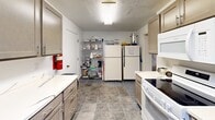 Located at 80 N Portage Path in Akron, Ohio, this single-floor community-style space offers a generous and flexible layout well-suited for gatherings, meetings, and events. The centerpiece is a large, open carpeted hall with a drop tile ceiling, recessed lighting, and skylights that brighten the interior. The hall accommodates multiple round and folding tables with chairs, making it highly adaptable for various event configurations. Display shelving lines one wall, adding character to the space. An adjacent area features accent walls in warm terracotta and deep purple tones, providing a more intimate setting for smaller gatherings or breakout sessions. This room also benefits from drop ceiling skylights and recessed lighting. The fully equipped kitchen is designed for high-volume food preparation, featuring ample cabinetry, generous countertop space, a full-size refrigerator, an electric range, a microwave, and durable tile flooring. Additional storage shelving makes the kitchen practical for event catering needs. Throughout the space, the blue patterned carpeting, neutral walls, and consistent drop ceilings create a cohesive and functional atmosphere. The layout offers excellent versatility for community programming, social events, and organizational meetings.