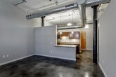 Located at 108 Walnut St in the heart of Kansas City, MO, this urban loft-style unit masterfully blends industrial character with modern finishes across a single open floor plan. Soaring ceilings with exposed metallic ductwork and ceiling fans set the tone throughout the main living area, which is anchored by richly polished concrete floors that extend seamlessly from room to room. A standout feature of the living space is a full wall of original exposed brick, adding warmth and historic texture to the otherwise contemporary palette of cool gray tones.

The kitchen is thoughtfully designed with dark espresso cabinetry reaching to the ceiling, stone-look countertops, a classic subway tile backsplash, and stainless steel appliances including a full-size refrigerator. A peninsula counter opens directly to the living area, creating a natural flow ideal for both everyday living and entertaining. Track and pendant lighting throughout provides targeted illumination to complement the industrial aesthetic.

A private bedroom area features the same polished concrete flooring and exposed brick accent wall, lending cohesion to the overall design. The bathroom is clean and functional, outfitted with matching dark cabinetry, a wide vanity mirror, and a walk-in shower. The unit's industrial-modern design makes it a distinctive offering in Kansas City's vibrant downtown district.