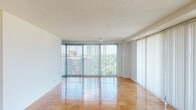 Located at 110 W 39th Street in Baltimore, MD, this single-floor residence offers a well-organized layout that balances open living spaces with functional private areas. The expansive living and dining areas are defined by gleaming parquet flooring and wall-to-wall floor-to-ceiling windows dressed with vertical blinds, allowing abundant natural light to pour in while framing elevated views of the surrounding urban skyline and tree canopy. A sliding glass door provides direct access to a balcony, extending the living space outdoors. The bedroom is generously sized, continuing the warm parquet flooring and featuring a wide sliding-door closet for ample storage. The kitchen is efficiently designed with light wood cabinetry, dark countertops, a blue tile backsplash, and stainless steel appliances including a gas range, dishwasher, and refrigerator. Additional shelving and utility space are also present in the kitchen area. The bathroom is clean and functional, equipped with a combined tub and shower, a toilet, and a vanity with light wood cabinetry, a wide mirror, and under-sink storage. Textured ceilings throughout lend a classic mid-century character to the space, while the overall layout offers a comfortable, light-filled living environment in a convenient Baltimore location.