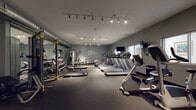 Located at 38401 Mentor Ave in Willoughby, Ohio, this fitness center offers a well-equipped, single-floor workout facility designed to support a full range of exercise routines. The space features a dark rubberized flooring throughout, providing a durable and functional surface suited for both cardio and strength training activities.

The cardio section is prominently equipped with multiple treadmills arranged in a row, each accompanied by wall-mounted televisions for entertainment during workouts. An elliptical trainer and a recumbent stationary bike round out the cardio offerings, providing varied low-impact exercise options.

The strength training area includes a multi-station cable machine, a dumbbell rack stocked with a wide range of free weights, and a weight bench, all positioned alongside a large wall mirror that enhances visibility and spatial openness. Exposed ductwork along the ceiling adds an industrial character to the design.

Overhead track lighting illuminates the entire space effectively, ensuring consistent brightness throughout. Natural light filters in through frosted windows along the walls, complementing the artificial lighting. Near the entrance, a hand sanitizer station and a water dispenser are conveniently available to users. The layout is open and organized, allowing for comfortable movement between equipment zones.