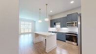 Located at 525 Sawnee Village Boulevard in Cumming, GA, this well-appointed one-bedroom, two-bathroom residence offers a thoughtfully designed single-level layout. The open-concept kitchen and living area serves as the heart of the home, anchored by a striking kitchen outfitted with slate-blue cabinetry, gold-toned hardware, stainless steel appliances, a geometric tile backsplash, and light quartz countertops. A central island with built-in shelving provides additional prep and storage space, while pendant lights with brass accents add a modern touch overhead. Light wood-tone flooring flows throughout the main living area, enhancing the bright and airy atmosphere created by large windows. The spacious primary bedroom features plush carpeting, a ceiling fan, and a generously sized window offering views of the surrounding greenery. A dedicated closet provides ample storage. Both bathrooms are finished with large-format tile flooring and clean, contemporary fixtures — one featuring a soaking tub with shower combo, and the other with a single-sink vanity with a wood-framed mirror and lighted fixture. Throughout the residence, neutral tones, recessed lighting, and clean architectural lines create a cohesive, modern aesthetic.