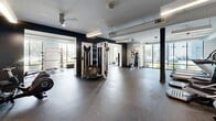 Located at 6854 Governors West NW in Huntsville, Alabama, this fitness center offers a thoughtfully designed, single-floor exercise facility with a generous and open layout. The space is divided into distinct functional zones, each outfitted with professional-grade equipment to support a wide range of workout routines.

The cardio area features multiple treadmills and elliptical machines positioned alongside large windows that flood the space with natural light and provide views of the surrounding exterior. Wall-mounted televisions above the cardio equipment add convenience for users during extended sessions. Ceiling fans maintain comfortable airflow throughout.

A dedicated strength and free weights zone includes a full rack of dumbbells, weight benches, and a multi-function cable machine, all set against accent walls in deep navy, creating a bold and motivating atmosphere. Mirrored walls enhance the sense of space and allow for proper form checks during exercise.

A separate, enclosed area accommodates additional specialty equipment including spin bikes, seated strength machines, and resistance apparatus, with floor-to-ceiling windows offering bright, open sightlines to the outdoors.

Throughout the facility, durable rubber flooring provides safety and comfort underfoot, while exposed ductwork along the ceiling contributes to the space's modern, industrial aesthetic. Structural columns are integrated cleanly into the layout, maintaining an unobstructed and functional workout environment.