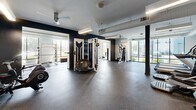 Located at 6854 Governors West NW in Huntsville, Alabama, this fitness center offers a thoughtfully designed, single-floor exercise facility with a generous and open layout. The space is divided into distinct functional zones, each outfitted with professional-grade equipment to support a wide range of workout routines.

The cardio area features multiple treadmills and elliptical machines positioned alongside large windows that flood the space with natural light and provide views of the surrounding exterior. Wall-mounted televisions above the cardio equipment add convenience for users during extended sessions. Ceiling fans maintain comfortable airflow throughout.

A dedicated strength and free weights zone includes a full rack of dumbbells, weight benches, and a multi-function cable machine, all set against accent walls in deep navy, creating a bold and motivating atmosphere. Mirrored walls enhance the sense of space and allow for proper form checks during exercise.

A separate, enclosed area accommodates additional specialty equipment including spin bikes, seated strength machines, and resistance apparatus, with floor-to-ceiling windows offering bright, open sightlines to the outdoors.

Throughout the facility, durable rubber flooring provides safety and comfort underfoot, while exposed ductwork along the ceiling contributes to the space's modern, industrial aesthetic. Structural columns are integrated cleanly into the layout, maintaining an unobstructed and functional workout environment.