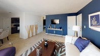 This single-floor residence offers a well-designed layout that balances comfort and style across its key living spaces. The living room serves as the central hub, featuring a bold navy accent wall, plush carpeting, and a sliding glass door that frames breathtaking water views and leads to an outdoor patio. Natural light pours in through sheer curtains, enhancing the open, airy feel of the space.

Adjacent to the living area, the dining space accommodates a round glass-top table beneath a pendant light fixture, with a nearby window adding natural brightness. The kitchen is equipped with dark espresso cabinetry, light countertops, tile flooring, and a full suite of black appliances including a refrigerator, dishwasher, and stove.

The primary bedroom features a dramatic navy accent wall, soft carpeting, and a sliding closet for ample storage. The second bedroom is finished in cool grey tones with carpet flooring, a built-in closet with open shelving, and a large window. The bathroom includes tile flooring, a dark vanity with a white countertop, and a shower-tub combination. Textured ceilings are consistent throughout the unit.
