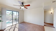This single-floor, one-bedroom, one-bathroom residence offers a practical and comfortable layout across a compact yet efficient floor plan. The living room is bright and inviting, featuring plush carpeting, a ceiling fan with a light fixture, and a sliding glass door that opens to a balcony with views of the surrounding landscape, including palm trees and a pool area, allowing abundant natural light to fill the space.

The bedroom is a well-proportioned retreat, also finished with soft carpeting and its own ceiling fan. A window fitted with horizontal blinds provides natural light and ventilation. A dedicated closet adds convenient storage to the room.

The kitchen is efficiently designed with warm wood cabinetry, laminate countertops, a double-basin sink, and white appliances including a refrigerator, dishwasher, stove, and microwave. Light tile flooring runs throughout the kitchen area, offering a clean and practical surface.

The bathroom is neatly appointed with a combination tub and shower, a toilet, and a vanity topped with granite-style countertops and a large mirror, providing functional and tidy facilities.

Throughout the home, neutral wall tones and consistent finishes create a cohesive and move-in-ready atmosphere suitable for comfortable everyday living.