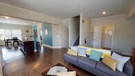 This three-story residence is designed with a practical and cohesive layout, finished throughout with rich, dark hardwood flooring that adds warmth and continuity across all levels. A staircase with wood-tread steps and white painted risers connects the floors, complemented by clean white railings and neutral-toned walls that keep the interior feeling bright and open.

The main living level offers an open-concept arrangement where the living room, dining area, and kitchen flow naturally into one another. The living room features a tray ceiling with a ceiling fan, large windows that bring in natural light, and ample space for seating. The adjacent dining area is equally well-lit, with multiple windows offering outdoor views. The kitchen is a standout feature, centered around a bold teal peninsula with granite-style countertops, seating for several, rich dark cabinetry, and stainless steel appliances including a refrigerator and microwave.

The upper level hosts a comfortable bedroom with a ceiling fan, a walk-in closet, and access to a full bathroom equipped with a soaking tub, shower, dark vanity with granite countertops, and hardwood flooring. A dedicated laundry area houses a full-sized washer and dryer alongside a water heater, adding everyday convenience. Hallways on the upper floors are wide and well-lit with recessed lighting.