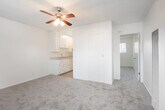 Located along East Pacific Coast Highway in Long Beach, California, this efficiently designed one-bedroom, one-bathroom unit makes smart use of its cozy footprint. The open living area features soft wall-to-wall carpeting and a ceiling fan with a light fixture overhead, creating a comfortable and functional main living space. A textured ceiling runs throughout, lending a consistent aesthetic across the unit. Seamlessly connected to the living area, the galley-style kitchen is outfitted with white upper and lower cabinetry, a double-basin stainless steel sink, and light-toned countertops, all set over easy-care vinyl plank flooring. A vertical panel wall divides the kitchen from the living space, adding a subtle architectural detail. The bedroom features plush carpeting, two closets — one a mirrored sliding-door style with built-in shelving — along with two wall switches and ample room to arrange furnishings. The bathroom is bright and well-appointed, with a white vanity, open wall shelving, a mirrored medicine cabinet, a tub/shower combination, and a frosted privacy window that allows natural light to filter in. The overall ambiance is clean, neutral, and move-in ready.