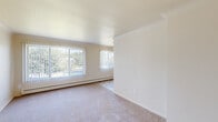 This single-floor unit in Washington, MI offers a practical and comfortable layout designed for efficient everyday living. The living area is bright and open, featuring neutral-toned carpet flooring and multiple windows dressed with vertical blinds that invite abundant natural light and outdoor views of surrounding greenery. Baseboard heating runs along the exterior walls throughout the space, ensuring consistent warmth. The open layout connects the living area to the rest of the unit seamlessly, as illustrated by the 3D floor plan.

The bedroom is a quiet, carpeted room with a window providing additional natural light and a full-width double bifold closet, offering ample storage space. Neutral wall tones and clean lines give the room a simple, functional character.

The kitchen features white cabinetry above and below the counter, a dark laminate countertop with a stainless steel sink, and tile-style flooring. White appliances include a coil-burner electric range and a full-size refrigerator. An overhead ventilation hood completes the functional cooking space. The overall ambiance of the unit is clean, bright, and move-in ready.