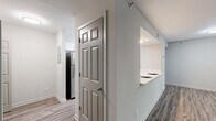 This well-organized single-story unit offers a practical and comfortable layout across its one bedroom and one bathroom. The living room serves as the central gathering space, featuring a fireplace framed in a dark surround and multiple windows with blinds that allow natural light to fill the room. A sliding glass door provides additional light and access to the exterior. Wood-style plank flooring runs throughout the living area and hallway, lending a cohesive, modern aesthetic.

The kitchen connects to the living area via a pass-through opening, enhancing the sense of openness. It is equipped with white cabinetry, light quartz-style countertops, a gray subway tile backsplash, and stainless steel appliances including a dishwasher and refrigerator. A closet within the kitchen area provides convenient pantry or storage space.

The bedroom is carpeted for comfort, features a large window with views of surrounding greenery, and connects directly to a hallway with a closet featuring louvered doors. The bathroom includes a vanity with light countertops, a toilet, and a tub-shower combination. A hallway with additional storage connects all rooms, completing this efficiently designed single-floor residence.