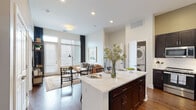 Located at Riverwalk in Plainsboro, NJ, this thoughtfully designed single-floor residence offers a seamless blend of modern finishes and comfortable living. The open-concept layout connects the kitchen and living area, creating an inviting, airy atmosphere filled with natural light from large windows dressed with stylish blinds and floor-to-ceiling curtains.

The kitchen is a standout feature, boasting rich dark cabinetry, stainless steel appliances, a subway tile backsplash, and a generous island with striking white quartz countertops — ideal for dining and entertaining. Hardwood floors flow throughout the main living areas, adding warmth and continuity.

The living room is bright and welcoming, with tall windows and direct access to an exterior door, enhancing the sense of openness. Multiple bedrooms offer plush carpeting, ample natural light, and generous closet space, including a walk-in closet accessible from the bathroom.

The primary bathroom is elegantly appointed with a dual-sink vanity featuring quartz countertops, dark cabinetry, an illuminated mirror, a glass-enclosed walk-in shower with white subway tile, and open built-in shelving. An in-unit stacked washer and dryer adds everyday convenience. The overall aesthetic is clean, contemporary, and refined throughout.