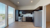 This contemporary single-floor unit offers a thoughtfully designed open-concept layout that combines the living area and kitchen into one bright, cohesive space. Large floor-to-ceiling windows along one wall flood the interior with natural light and provide open views of the surrounding neighborhood, enhancing the airy feel of the space. The light wood-style flooring in the main living area adds warmth and continuity throughout.

The kitchen is well-appointed with dark espresso-toned cabinetry that extends from floor to ceiling, offering generous storage. A full suite of stainless steel appliances includes a refrigerator, electric range, over-the-range microwave, and dishwasher, complemented by light-toned countertops and a single-basin sink. Recessed lighting overhead ensures the kitchen remains bright and functional.

The bedroom is a calm, neutral retreat finished with soft carpeting underfoot and clean white walls. A distinctive sliding barn door adds a modern architectural touch while providing a stylish transition between the bedroom and the main living space.

The bathroom features light wood-style flooring that mirrors the rest of the unit, with a full soaking tub and shower combination, a toilet, and a dark wood vanity cabinet that echoes the kitchen's design palette. The overall aesthetic throughout the unit is clean, modern, and cohesive.