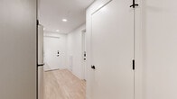 Located at 1704 N 17th St in Tampa, FL, this modern two-bedroom, two-bathroom residence offers a thoughtfully designed single-floor layout that maximizes every square foot of its compact footprint. Light-toned hardwood flooring flows throughout, complementing the clean white walls and recessed lighting that keep the space feeling bright and open.

The kitchen is efficiently arranged along a galley-style corridor, featuring stainless steel appliances including a range, microwave, and refrigerator, paired with gray cabinetry and light countertops. It connects seamlessly to the hallways that link each room.

The primary bedroom is the most expansive area of the home, highlighted by floor-to-ceiling windows that flood the room with natural light and provide views of the surrounding neighborhood. A built-in wall unit combines overhead cabinetry, an integrated TV mount, and a dedicated desk surface, offering both storage and a functional workspace. The second bedroom features a distinctive blue-gray accent wall, light wood flooring, and a cozy, well-defined layout.

Both bathrooms maintain a consistent modern aesthetic, with large-format tile flooring, floating vanities, matte black hardware accents, and glass-enclosed walk-in showers. The hallways connecting each room are clean and uncluttered, reinforcing the home's minimalist, contemporary character.
