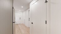 Located at 1704 N 17th St in Tampa, FL, this modern two-bedroom, two-bathroom residence offers a thoughtfully designed single-floor layout that maximizes every square foot of its compact footprint. Light-toned hardwood flooring flows throughout, complementing the clean white walls and recessed lighting that keep the space feeling bright and open.

The kitchen is efficiently arranged along a galley-style corridor, featuring stainless steel appliances including a range, microwave, and refrigerator, paired with gray cabinetry and light countertops. It connects seamlessly to the hallways that link each room.

The primary bedroom is the most expansive area of the home, highlighted by floor-to-ceiling windows that flood the room with natural light and provide views of the surrounding neighborhood. A built-in wall unit combines overhead cabinetry, an integrated TV mount, and a dedicated desk surface, offering both storage and a functional workspace. The second bedroom features a distinctive blue-gray accent wall, light wood flooring, and a cozy, well-defined layout.

Both bathrooms maintain a consistent modern aesthetic, with large-format tile flooring, floating vanities, matte black hardware accents, and glass-enclosed walk-in showers. The hallways connecting each room are clean and uncluttered, reinforcing the home's minimalist, contemporary character.