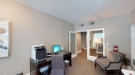 Located at 100 Crescent Arbor Ln in Cary, NC, this single-floor space offers a well-organized and functional layout designed for both productivity and comfort. The interior is finished in soft, neutral tones — warm greige walls paired with light-colored ceilings — creating a calm and professional ambiance throughout.

The workspace area is thoughtfully equipped, featuring a dark wood desk that accommodates a desktop computer and multifunction printer, making it well-suited for office use. A cushioned desk chair and a small wastebasket complete the practical setup. The carpeted flooring adds warmth underfoot and contributes to the overall quiet atmosphere of the space.

Slatted ceiling vents indicate a central HVAC system for year-round climate control. The space benefits from an open, connected layout — French-style double doors with glass panes lead to an adjacent room, and a hallway beyond provides further access to additional areas. Through the glass doors, a sleeping area with a bedside lamp and upholstered seating is visible, suggesting a suite-style configuration.

The smooth white door and trim work contrast cleanly against the neutral walls, lending the space a polished, finished look. Overall, this space combines a clean aesthetic with practical design elements to support a comfortable and efficient environment.