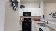 This single-floor residence offers a thoughtfully designed layout that balances comfort and functionality throughout. The kitchen is a standout feature, showcasing crisp white shaker-style cabinetry extending to the ceiling, granite-style countertops, wood-look flooring, and black appliances including a range, built-in microwave, dishwasher, and double-basin sink. A curved breakfast bar provides a seamless transition into the open living and dining area, creating an inviting, connected atmosphere ideal for everyday living and entertaining.

The living room is bright and welcoming, with wood-look flooring, neutral walls, and large windows dressed with sheer curtains that allow natural light to filter through while offering views to the outdoors. A sliding glass door leads to an exterior access point, further enhancing the sense of openness.

The bedroom features plush carpet, a ceiling fan, and a window that brings in natural light. It is complemented by a well-sized bathroom with a vanity, granite-style countertop, and wood-look flooring. A spacious walk-in closet is conveniently accessible from the bathroom, offering generous storage. A secondary bathroom includes a combination tub and shower with clean tile surround. Throughout, the design palette of soft neutrals and light tones creates a cohesive, comfortable living environment.