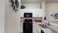 This single-floor residence offers a thoughtfully designed layout that balances comfort and functionality throughout. The kitchen is a standout feature, showcasing crisp white shaker-style cabinetry extending to the ceiling, granite-style countertops, wood-look flooring, and black appliances including a range, built-in microwave, dishwasher, and double-basin sink. A curved breakfast bar provides a seamless transition into the open living and dining area, creating an inviting, connected atmosphere ideal for everyday living and entertaining.

The living room is bright and welcoming, with wood-look flooring, neutral walls, and large windows dressed with sheer curtains that allow natural light to filter through while offering views to the outdoors. A sliding glass door leads to an exterior access point, further enhancing the sense of openness.

The bedroom features plush carpet, a ceiling fan, and a window that brings in natural light. It is complemented by a well-sized bathroom with a vanity, granite-style countertop, and wood-look flooring. A spacious walk-in closet is conveniently accessible from the bathroom, offering generous storage. A secondary bathroom includes a combination tub and shower with clean tile surround. Throughout, the design palette of soft neutrals and light tones creates a cohesive, comfortable living environment.