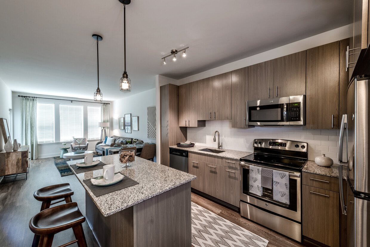 Open concept kitchen with brown cabinetry, granite countertops, kitchen island, stainless steel appliances, tile backsplash and hard surface flooring - Avalon Arundel Crossing