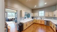 Located at 108 Cottage Creek Rd SW in Huntsville, Alabama, this single-story space offers a well-organized layout combining a fully equipped kitchen and an inviting living room. The kitchen is a standout feature, outfitted with light natural wood cabinetry paired with matte black hardware, bright white countertops, and warm hardwood flooring that extends throughout the space. Stainless steel appliances — including a range, dishwasher, refrigerator, and microwave — provide a modern, functional aesthetic. A pass-through window connects the kitchen to the adjacent dining and living areas, fostering an open, communicative flow between spaces.

The living room is distinguished by rich blue-gray walls that create a bold, cohesive atmosphere. A tray ceiling with recessed lighting and a decorative chandelier adds architectural depth overhead, while large windows allow natural light to fill the room and offer views of the surrounding neighborhood. Open shelving along the walls provides both display and storage opportunities. A separate dining area with hardwood flooring and direct sightlines into the kitchen completes the layout. Together, the rooms create a practical, stylish, and connected environment well-suited for everyday use and gathering.