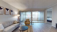 This single-floor residence is designed with a clean, contemporary aesthetic, combining functional layouts with modern finishes. Light wood-look flooring runs throughout the space, creating a cohesive and airy feel across every room.

The living area serves as the centerpiece of the unit, offering generous space for seating and relaxation. A wall of sliding glass doors with vertical sheer panels floods the room with natural light and provides access to an outdoor area, where views of mature trees create a tranquil backdrop. Crown molding and a textured ceiling add architectural detail to the space.

The galley-style kitchen is well-appointed with two-toned gray cabinetry, granite countertops, white subway tile backsplash, and a full suite of stainless steel appliances, including a refrigerator, range, dishwasher, and range hood. The layout maximizes efficiency while maintaining a polished appearance.

The two bedrooms are calm and neutrally toned, each featuring light gray walls, wood-look flooring, and ample natural light. One bedroom includes a sliding glass door, while both offer closet storage. The bathroom is finished with a granite-topped vanity, a tiled tub-shower combination, and wood-look flooring, maintaining the consistent style found throughout the home.