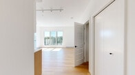 This thoughtfully designed 1-bedroom, 1-bathroom unit offers a clean, modern aesthetic throughout its single floor of living space. The open-concept living and kitchen area is bright and airy, featuring warm light hardwood flooring, crisp white walls, and a combination of recessed and track lighting overhead. Large floor-to-ceiling windows and a sliding glass door flood the living area with natural light and provide access to a balcony, framing pleasant treetop and neighborhood views.

The kitchen is well-appointed with a two-tone cabinetry design — white upper cabinets paired with light wood lower cabinets — complemented by sleek white quartz countertops, a tiled backsplash, and a full suite of stainless steel appliances including a refrigerator, electric range, built-in microwave, and dishwasher.

The bedroom is a serene, sun-drenched retreat with a generously sized window that captures expansive views of the surrounding neighborhood and greenery, with baseboard heating ensuring year-round comfort.

The bathroom features a clean, contemporary design with warm wood-tone flooring, a floating white vanity, and a full tub-shower combination finished with elegant vertically laid grey tile. A hallway connects the spaces efficiently, completing this well-organized and stylish unit.