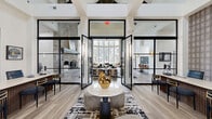 Located at 1333 Eldridge Pkwy in Houston, TX, this beautifully appointed single-floor community clubhouse delivers a sophisticated blend of architectural character and modern design across a generously sized footprint. The grand entrance welcomes visitors through striking steel-framed glass doors into a central lounge defined by soaring vaulted ceilings with exposed dark wood trusses, light hardwood flooring, and an abundance of natural light. A dramatic floor-to-ceiling stone fireplace serves as a focal point, complemented by curated furnishings and contemporary art throughout. Expansive multi-pane windows frame outdoor views of the surrounding grounds and pool area, enhancing the open, airy ambiance. The lounge flows seamlessly into a bar-height seating area, ideal for social gatherings. The kitchen features warm wood cabinetry, white quartz countertops, stainless steel appliances, and eye-catching teal geometric tile. Three private offices offer functional workspaces, including a conference-style room with a marble oval table and velvet seating, and individual offices with slatted wood wainscoting. The fitness center boasts vaulted ceilings, full-length mirrors, ample natural light, cardio and strength equipment, and direct access to the pool area.