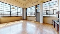 This industrial loft at 2320 E Superior Ave in Cleveland's North Shore neighborhood showcases a striking conversion aesthetic with soaring ceilings, exposed concrete columns, and visible ductwork running throughout the space. The open-plan living area is anchored by large, multi-pane factory-style windows that flood the hardwood floors with abundant natural light and offer urban skyline views. Pendant light fixtures with a vintage industrial character complement the raw architectural details, including original concrete surfaces and structural columns.

The kitchen is integrated into the main living space and features dark wood cabinetry, stainless steel appliances including a range, microwave, dishwasher, and refrigerator, set against a continuous countertop with a utility sink.

Both bedrooms offer generous proportions, with the primary bedroom providing ample square footage, a closet with built-in rod, and a pendant light. Each bedroom benefits from natural light streaming through large windows.

The two bathrooms are functionally appointed: one features a navy vanity with a wall-mounted mirror, open wood shelving, and tile flooring, while the other includes a stand-up shower. A hallway connects the private areas of the unit, completing this well-structured urban loft.