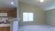 Located at 312 Foxtail Dr. in Pataskala, Ohio, this single-story home offers a thoughtfully designed open-concept layout that maximizes both space and functionality. The living area is a standout feature, boasting soaring vaulted ceilings that lend an expansive, airy feel to the room. A large window allows an abundance of natural light to pour in, illuminating the neutral-toned carpet and soft green walls that create a calm, welcoming atmosphere. A ceiling fan is positioned above, adding both practicality and a subtle decorative touch. The living space flows seamlessly into the kitchen area, which is defined by a raised breakfast bar countertop — an ideal spot for casual dining or entertaining. Warm wood-toned cabinetry lines the kitchen, providing ample storage while complementing the home's overall neutral palette. The open sightlines between the kitchen and living room enhance the sense of connectivity throughout the main living areas. Clean white trim and baseboards add a crisp, finished look throughout the space. The single-floor design ensures easy accessibility and a cohesive living experience from room to room, making this home both practical and comfortable.