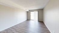 This single-floor unit offers a clean, contemporary layout designed for comfortable everyday living. The open living area is finished with durable wood-look plank flooring in a soft gray tone and features a sliding glass door dressed with vertical blinds, filling the space with natural light and providing access to an outdoor area. A hallway connects the main living zone to the private areas of the unit, maintaining a logical and functional flow throughout.

The kitchen showcases updated finishes including crisp white cabinetry with matte black hardware, a deep stainless steel undermount sink, and striking quartz countertops with subtle veining. A neutral subway tile backsplash adds texture, while a built-in microwave and dishwasher contribute to the space's practical appeal.

The bedrooms are carpeted for warmth and comfort, with neutral wall tones and ample wall space. One bedroom features a ceiling fan with light fixture and a window offering an outdoor view, enhancing both ventilation and natural light. The bathroom is finished with large-format stone-look wall tiles surrounding a full soaking tub and shower combination, lending a clean and polished aesthetic. Throughout the unit, consistent neutral tones, textured ceilings, and clean white trim create a cohesive and move-in ready environment.
