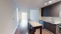 This two-story residence offers a thoughtfully designed layout spread across two levels, providing a comfortable and functional living environment. The main floor features an open-concept kitchen and living area, where hardwood-style flooring flows seamlessly throughout. The kitchen is outfitted with dark espresso cabinetry, granite countertops, subway tile backsplash, stainless steel appliances including a refrigerator, range, microwave, and dishwasher, and a central island that doubles as a prep and dining space. Track lighting illuminates the kitchen, while the adjacent living area benefits from tall ceilings and a large vertical-blind window that invites abundant natural light. A staircase connects the main floor to the upper level, which houses the private bedroom. The bedroom features plush carpeting, a sliding barn-style door, and a window with natural light. It provides direct access to a hallway leading to the full bathroom, which is equipped with a tub-shower combo with white tile surround and brushed nickel fixtures. The upper level also includes a loft-style area with carpeted flooring, a ceiling fan, and an open railing overlooking the lower level, adding architectural character to the home.
