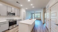 Located at 55 Caldwell Dr in Mount Holly, NC, this well-appointed 3-bedroom, 2-bathroom single-story home offers a thoughtfully designed open-concept layout with modern finishes throughout. The heart of the home is a sleek kitchen featuring gray shaker-style cabinetry, a classic white subway tile backsplash, stainless steel appliances including a refrigerator with ice maker, range, and built-in microwave, as well as a generous center island with a white quartz countertop, undermount sink, and integrated outlets. The kitchen flows seamlessly into a bright living room with wood-look plank flooring, a ceiling fan, and large windows and a glass door that invite abundant natural light and outdoor views. The spacious primary bedroom features wood-look flooring, a ceiling fan, and windows overlooking greenery, while the en suite bathroom offers gray vanity cabinetry, a white quartz countertop, and a glass-enclosed tiled shower. The two additional bedrooms are finished with plush carpet, ceiling fans, and natural light. A second full bathroom provides a single vanity with matching finishes. A dedicated walk-in closet with wire shelving adds practical storage. Clean white walls and consistent modern finishes lend the home a cohesive, contemporary ambiance throughout.
