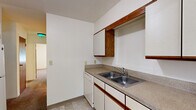 Located at 1471 Burke Ave NE in Grand Rapids, Michigan, this single-floor unit offers three bedrooms, one bathroom, a living room, kitchen, and hallway — making efficient use of its compact footprint. The kitchen features white cabinetry with warm wood trim accents, granite-look laminate countertops, a double stainless steel sink, and a dishwasher, with tile flooring underfoot. Upper and lower cabinets provide ample storage, and an open pass-through connects the kitchen to the adjacent living area. The living room is carpeted and includes a window with blinds that brings in natural light and neighborhood views, along with baseboard heating. Each of the three bedrooms is finished with wall-to-wall carpet and neutral white walls. The primary bedroom is generously sized and features a closet with bifold doors. Additional bedrooms also benefit from windows with natural light and baseboard heating. The full bathroom includes white subway tile surrounding a tub/shower combo, a toilet, vanity sink, tile flooring, a window for ventilation and natural light, and a wood-toned storage cabinet above. A hallway connects the rooms, completing this straightforward and functional single-level layout.