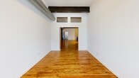 Located at 21 W North St in Akron, Ohio, this 2-bedroom, 2-bathroom loft-style residence blends industrial character with modern finishes across a generously sized single floor. The open-concept living, dining, and kitchen area serves as the heart of the home, showcasing rich hardwood flooring, bold exposed steel beams, and visible ductwork that speak to the building's industrial heritage. The kitchen is well-appointed with dark espresso cabinetry, granite countertops, stainless steel appliances including a gas range and refrigerator, a deep sink, and a breakfast bar with pendant lighting overhead. The spacious primary bedroom features soaring ceilings with exposed beams, large multi-pane windows framing outdoor views, and large-format tile flooring. An additional bedroom and a den provide flexible living options. Four closets throughout the unit offer generous storage. The two bathrooms are finished with dark wood vanities and granite or stone countertops — one features a glass-enclosed walk-in shower, while the other includes a full soaking tub. A dedicated utility room and a welcoming entrance complete the layout. Natural light flows through the oversized, classic-paned windows, enhancing the open and airy atmosphere of this distinctive urban residence.