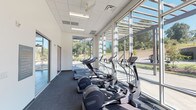 Located at 109 Anderson Hwy in Clemson, SC, this modern, single-story fitness facility is thoughtfully designed to accommodate a wide range of workout needs. The space is defined by its expansive floor-to-ceiling glass curtain walls, which flood the interior with natural light and offer open views of the surrounding landscape, creating an energizing atmosphere throughout.

The cardio zone lines the perimeter glass walls and is equipped with a row of treadmills, elliptical trainers, and stationary bikes, all oriented to take advantage of the outdoor views. Adjacent to this area, a dedicated strength training floor features a comprehensive dumbbell rack, cable machines, and resistance equipment, with large wall mirrors that enhance the sense of space. Durable carpet tile flooring and bold purple accent columns define this zone.

A separate functional training room, distinguished by vibrant orange accent walls and hardwood-style flooring, houses medicine balls, resistance cables, a pulley system, and an array of functional fitness accessories. Ceiling-mounted fans and mounted flat-screen televisions are found throughout the facility.

A cycling studio provides space for spin bikes alongside additional cardio equipment. Built-in storage cubbies and cabinetry offer practical organization solutions near the entrance. The facility's clean, contemporary design, high ceilings, and energetic color palette create a motivating and professional environment well-suited for fitness training.