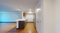 This one-bedroom, one-bathroom unit at 3035 NE 130th St in Seattle's vibrant NE neighborhood offers a well-designed layout across a single floor. Warm wood-style flooring flows throughout the living areas, complementing the clean, contemporary aesthetic of white walls and dark baseboards.

The open-concept living room and kitchen form the heart of the unit. The kitchen is appointed with stainless steel appliances, including a refrigerator, electric range, and microwave, alongside warm wood-toned upper cabinetry and dark lower cabinets. A peninsula with a white countertop provides additional prep space and casual seating. Track and recessed lighting illuminate the kitchen effectively.

The living room is a bright, airy space anchored by large windows that frame views of surrounding greenery, filling the room with natural light. A baseboard heating system runs along the exterior wall beneath the windows.

The bedroom is a comfortably sized retreat featuring its own large window with tranquil tree views, continuing the wood-style flooring, and a sliding double-door closet providing ample storage.

The bathroom is finished with clean white tile surrounding a full soaking tub and shower combination, accented by brushed nickel fixtures and a grab bar, offering a simple, functional design.