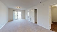 Located at 2620 Northchase Pkwy in Wilmington, North Carolina, this single-floor residence offers a clean, functional layout designed for comfortable everyday living. The living area is generously proportioned, finished with plush wall-to-wall carpeting and neutral-toned walls that create a bright, welcoming atmosphere. A pass-through window connects the living space to the kitchen, enhancing the open feel of the floor plan. The front entryway leads directly into the main living area, which benefits from natural light filtering through window treatments.

The kitchen features dark hardwood-style flooring, white cabinetry, a double-basin sink, and a freestanding range, providing a practical and well-organized cooking space. Adjacent areas offer additional storage and utility access.

The bedrooms are carpeted and finished with neutral walls, each receiving natural light through standard windows with blinds. The primary bedroom stands out with sliding glass doors that open to an outdoor balcony, offering views of the surrounding greenery, along with a built-in closet with rod and shelf storage.

The bathroom is clean and efficiently arranged, featuring a combination tub and shower with a white surround, a vanity with an integrated sink and large mirror, hardwood-style flooring, and a toilet — all presented in a bright, neutral palette.