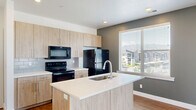 This well-appointed one-bedroom, one-bathroom residence offers a thoughtfully designed open-concept layout that maximizes its comfortable footprint. The combined kitchen and living area forms the heart of the space, showcasing warm wood-tone cabinetry extending to the ceiling for ample storage, white quartz countertops, a central island with an integrated sink, and a full suite of black Whirlpool appliances including a refrigerator, electric range, microwave, and dishwasher. A subway tile backsplash and recessed lighting add a clean, modern touch. Rich hardwood-style flooring flows throughout the main living areas, complemented by muted sage-green accent walls that create a calm, contemporary ambiance. Sliding glass doors in the living area open to a private balcony, flooding the space with natural light and providing open outdoor views. The bedroom continues the modern aesthetic with plush carpet, a large window, and its own sliding door access to the balcony. A spacious walk-in closet with built-in shelving and hanging rods offers generous storage. The bathroom features a wood-tone vanity with white quartz countertops, hardwood-style flooring, and a full bathtub with tiled surround. A dedicated closet with carpet completes the layout.