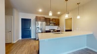 This well-designed single-floor residence offers a thoughtful layout that balances open communal spaces with comfortable private areas. The heart of the home is an open-concept kitchen and living area, where a generous island with a light quartz countertop and undermount sink serves as a natural gathering point. The kitchen is outfitted with rich dark wood cabinetry, a classic white subway tile backsplash, and a full suite of stainless steel appliances including a French door refrigerator with ice and water dispenser, gas range, and built-in microwave. Pendant lighting above the island adds a modern, polished touch. The adjacent living area features warm wood-look flooring that flows seamlessly throughout the main spaces, creating a cohesive and inviting atmosphere. A distinctive bold blue entry door provides a striking design accent. Bedrooms are carpeted for comfort, and the primary suite includes a walk-in closet equipped with wire shelving systems for ample storage. The bathrooms are clean and contemporary, with one featuring a glass-enclosed walk-in tile shower with floor-to-ceiling tile surround, and another offering a dark wood vanity with a white countertop. A dedicated laundry room with a full-size front-loading washer and dryer adds everyday convenience to this well-appointed residence.