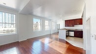 Located in the heart of Downtown Los Angeles on W 5th Street, this two-bedroom, two-bathroom residence offers a well-designed single-floor layout. Rich hardwood flooring flows throughout the open-concept living and dining area, which is bathed in natural light from large windows overlooking the surrounding cityscape. The kitchen is equipped with stainless steel appliances, including a refrigerator, range, and microwave, complemented by rich dark wood cabinetry and a granite-topped breakfast bar that connects seamlessly to the living space. Tile flooring grounds the kitchen area, creating a functional transition zone. The primary bedroom is generously proportioned, featuring hardwood floors, a mirrored sliding closet, and a large window that fills the room with natural light. It connects directly to a private en-suite bathroom finished in dramatic floor-to-ceiling marble tile, complete with a glass-enclosed shower. The second bathroom echoes this luxurious aesthetic with matching marble tile, a soaking tub, and dark wood vanity. The second bedroom also features hardwood floors and a bright window with urban views. Recessed lighting and clean white walls throughout contribute to a bright, modern ambiance.