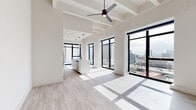 Located at 703 St. Joseph Pkwy in the heart of Houston, TX, this modern two-bedroom, two-bathroom residence offers a thoughtfully designed open-concept layout with impressive urban views. The expansive living and dining area is anchored by soaring ceilings with exposed structural elements and a ceiling fan, while oversized black-framed floor-to-ceiling windows flood the space with natural light and frame sweeping Houston skyline panoramas. Light wood-look flooring flows throughout the main living areas, enhancing the bright, airy ambiance. The sleek, contemporary kitchen features a large waterfall-edge island with an undermount sink, white cabinetry paired with warm wood-tone upper cabinets, stainless steel appliances, a gas range, a built-in wine cooler, and stylish pendant lighting. Both bedrooms are carpeted and receive generous natural light through large black-framed windows with city views. The primary bedroom includes a spacious walk-in closet outfitted with built-in shelving and hanging systems. The bathrooms are finished with modern wood-tone vanities, backlit mirrors, matte black fixtures, and marble-tiled shower surrounds. A dedicated laundry room with a full-size washer and dryer completes this well-appointed urban retreat.