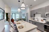 Located at 2501 Gunbarrel Rd in Chattanooga, TN, this one-bedroom, one-bathroom residence offers a thoughtfully designed single-floor layout that maximizes every square foot. The open-concept kitchen and living area serves as the heart of the home, anchored by a striking oversized island with quartz countertops and stylish pendant lighting overhead. The kitchen is outfitted with sleek gray cabinetry, a white geometric tile backsplash, stainless steel appliances including a French door refrigerator, and a black matte sink fixture — a combination that balances modern aesthetics with everyday functionality. Light wood-style flooring flows throughout the main living area, complementing the bright, neutral color palette. The living room receives generous natural light through large windows and features a ceiling fan, creating an airy and comfortable atmosphere. The bedroom is a quiet retreat, carpeted for warmth and comfort, with large windows that frame outdoor greenery and direct access to a walk-in closet. The full bathroom includes a soaking tub with shower, wood-look flooring, and connects conveniently to additional closet space. A dedicated laundry area and three closets round out the practical storage offerings throughout this well-appointed Chattanooga residence.