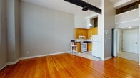 Located at 278 Main St in West Haven, CT, this studio offers a well-designed single-floor layout that blends industrial character with everyday functionality. The main living area is open and airy, showcasing rich, warm-toned hardwood flooring that extends throughout the space. An exposed black ductwork system runs along the ceiling, lending the unit a distinctive loft-inspired aesthetic. Large windows fitted with vertical blinds allow generous natural light to fill the room, creating a bright and inviting atmosphere.

The kitchen is efficiently arranged in an L-shaped configuration, featuring warm oak cabinetry, dark countertops, and white appliances including a gas range, dishwasher, and refrigerator. A pendant light hangs above, adding a functional and stylish touch to the cooking area. A small breakfast bar with seating provides a convenient spot for casual dining.

The bathroom is clean and practical, featuring a wood-toned vanity with a white countertop and sink, a large mirror with overhead lighting, and a shower-tub combination. Light tile flooring completes the space with a neutral, cohesive look. Overall, this studio combines an industrial-modern design sensibility with comfortable, practical living features.