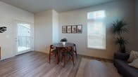 This well-designed single-floor residence combines modern finishes with a functional, open layout. The kitchen is a standout feature, showcasing rich dark wood cabinetry, gleaming granite-style countertops, a central island with pendant lighting, and a full suite of black appliances including a refrigerator, range, microwave, and dishwasher. Wood-look flooring runs throughout the main living areas, lending warmth and continuity to the space.

The open-concept design connects the kitchen seamlessly to the dining and living areas. The dining space accommodates a round table and chairs beneath a large window that allows natural light to pour in. The living room continues this bright, airy feel with expansive windows dressed in blinds and floor-length curtains, offering views of the surrounding neighborhood.

Multiple bedrooms provide comfortable retreats, each featuring plush carpeting, generous windows with outdoor views, and ample space for furnishings. Natural light is a recurring theme throughout, with windows positioned to brighten every room.

The bathrooms are clean and practical, each equipped with a full shower-tub combination, wood-look flooring, and a vanity with stone-style countertops. The overall aesthetic throughout the unit is contemporary and cohesive, with neutral tones creating a calm, inviting atmosphere.