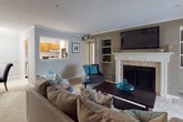 This thoughtfully designed single-floor residence offers a cohesive layout connecting comfortable living and dining spaces. The living room serves as a central hub, anchored by a tiled fireplace with a classic white mantle, built-in shelving, and a wall-mounted television. Crown molding and neutral-toned walls contribute to a refined yet relaxed atmosphere throughout, while plush carpeting runs consistently across the main living areas.

Adjacent to the living room, the dining area accommodates a round wooden table beneath track lighting, with crown molding continuing the space's polished aesthetic. A pass-through window connects seamlessly to the galley-style kitchen, which features warm wood cabinetry, stone-tiled flooring, and stainless steel appliances including a gas range and refrigerator. A laundry closet is conveniently accessible from within the kitchen.

A standout feature is the den enclosed by elegant French doors, offering abundant natural light through multiple windows framed by patterned drapes and a ceiling fan overhead — ideal as a home office or flexible living space.

The primary bedroom includes sliding glass door access to a private balcony with outdoor views, while a second bedroom benefits from vaulted ceilings and generous natural light. The bathroom features wood-toned cabinetry and a wide vanity with ample counter space.