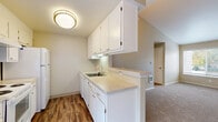 This well-designed 1-bedroom, 1-bathroom residence offers an efficient and comfortable layout across a single floor. The combined kitchen and living area forms the heart of the home, where vaulted ceilings with angled walls create a sense of openness well beyond the unit's compact footprint. The living room features neutral-toned carpet, a ceiling fan, and a sliding glass door that fills the space with natural light and provides access to the outdoors. The kitchen is laid out in a galley style, featuring white cabinetry extending to the ceiling, light countertops, a double-basin sink, and white appliances including a coil-top range and refrigerator. A peninsula counter separates the kitchen from the living area, adding a casual dining or prep space. The bedroom is carpeted and bathed in natural light from corner windows with exterior views, and includes two closets — one with mirrored sliding doors — offering generous storage. The full bathroom is finished with wood-look flooring, a white vanity with storage, a large mirror, and a tub-shower combination. Additional conveniences include a dedicated laundry space, a hallway connecting the private areas, and three closets throughout the unit for abundant storage.