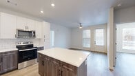 Located in Denver's vibrant Central Park neighborhood, this thoughtfully designed single-floor residence offers three bedrooms, two bathrooms, a kitchen, a living room, and a closet. The open-concept kitchen is a standout feature, showcasing two-tone cabinetry with dark lower and white upper cabinets, a classic white subway tile backsplash, stainless steel appliances, and a center island with a crisp white countertop. A stacked washer and dryer unit is conveniently integrated into the kitchen area. The kitchen flows seamlessly into the living room, which benefits from natural light through large windows and a ceiling fan. Each bedroom is finished with warm-toned hardwood-style flooring, bright white walls, and generous windows fitted with blinds that invite natural light while maintaining privacy. The spacious primary bedroom includes a walk-in closet outfitted with wire shelving and hanging rods for ample storage. The bathroom features floor-to-ceiling white subway tile surrounding a soaking tub and shower combination, accented by matte black hardware. Consistent light wood-tone flooring, recessed lighting, and a clean, neutral palette create a cohesive and modern ambiance throughout the entire home.