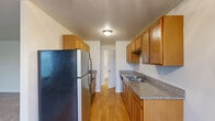 Located at 11200 SW Greenburg Rd in Tigard, Oregon, this one-bedroom, one-bathroom residence offers a practical and comfortable single-floor layout. The living room is the heart of the unit, featuring soft carpet flooring, a soothing sage green accent wall, and multiple windows — including a sliding glass door leading to a balcony — that fill the space with natural light and provide views of the surrounding neighborhood. A wall-mounted HVAC unit ensures year-round climate control. The galley-style kitchen is efficiently designed with warm oak cabinetry offering ample upper and lower storage, granite-look countertops, a double-basin sink, and durable hardwood flooring. Appliances include a full-size refrigerator, oven/range, and dishwasher. A hallway connects the main living areas to the private bedroom, which is carpeted and features a window with neighborhood views, a dedicated closet, and neutral wall tones that create a calm, restful atmosphere. The bathroom is equipped with a combination tub and shower enclosed by sliding frosted glass doors with chrome hardware. The unit's clean, neutral palette and functional layout make it a well-organized living space in a convenient Tigard location.